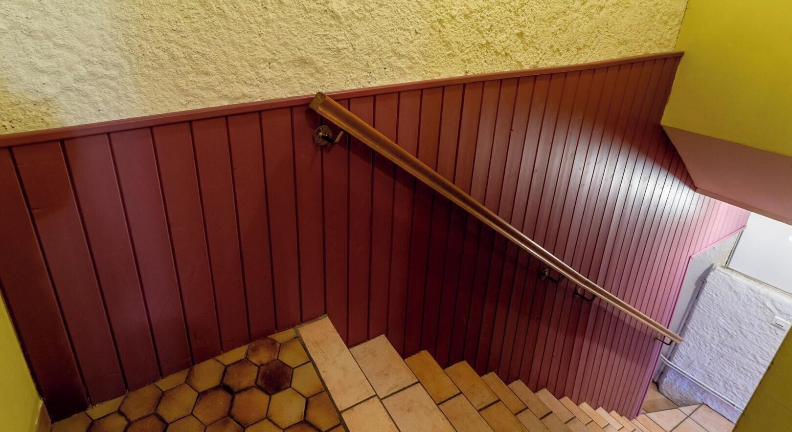 A wooden staircase with a handrail, a textured wall, and a tiled floor.