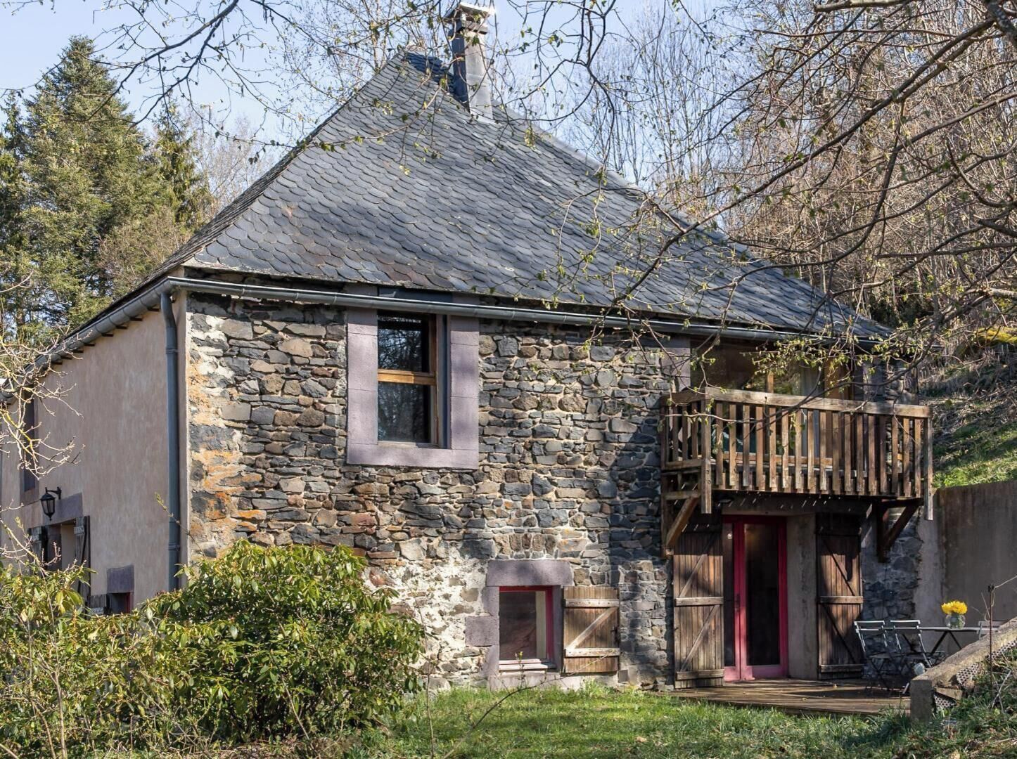 Une maison en pierre avec un toit en pente, une petite fenêtre et un balcon en bois.