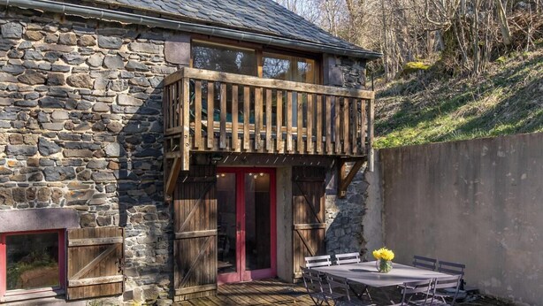 A stone building with a wooden balcony, a table with chairs, and a vase with flowers.