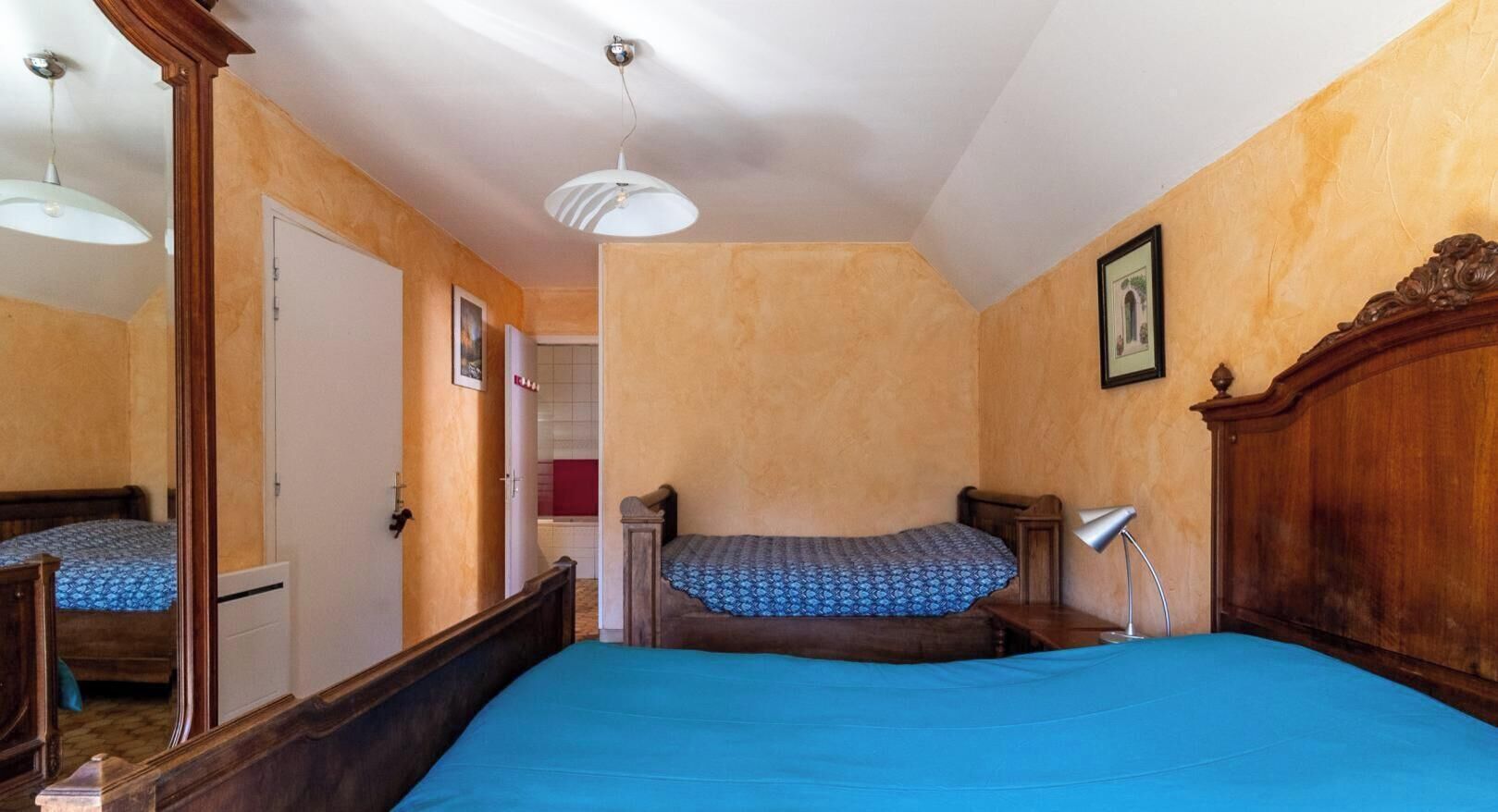 Un dormitorio con cama, mesita de noche, lámpara, espejo y puerta.