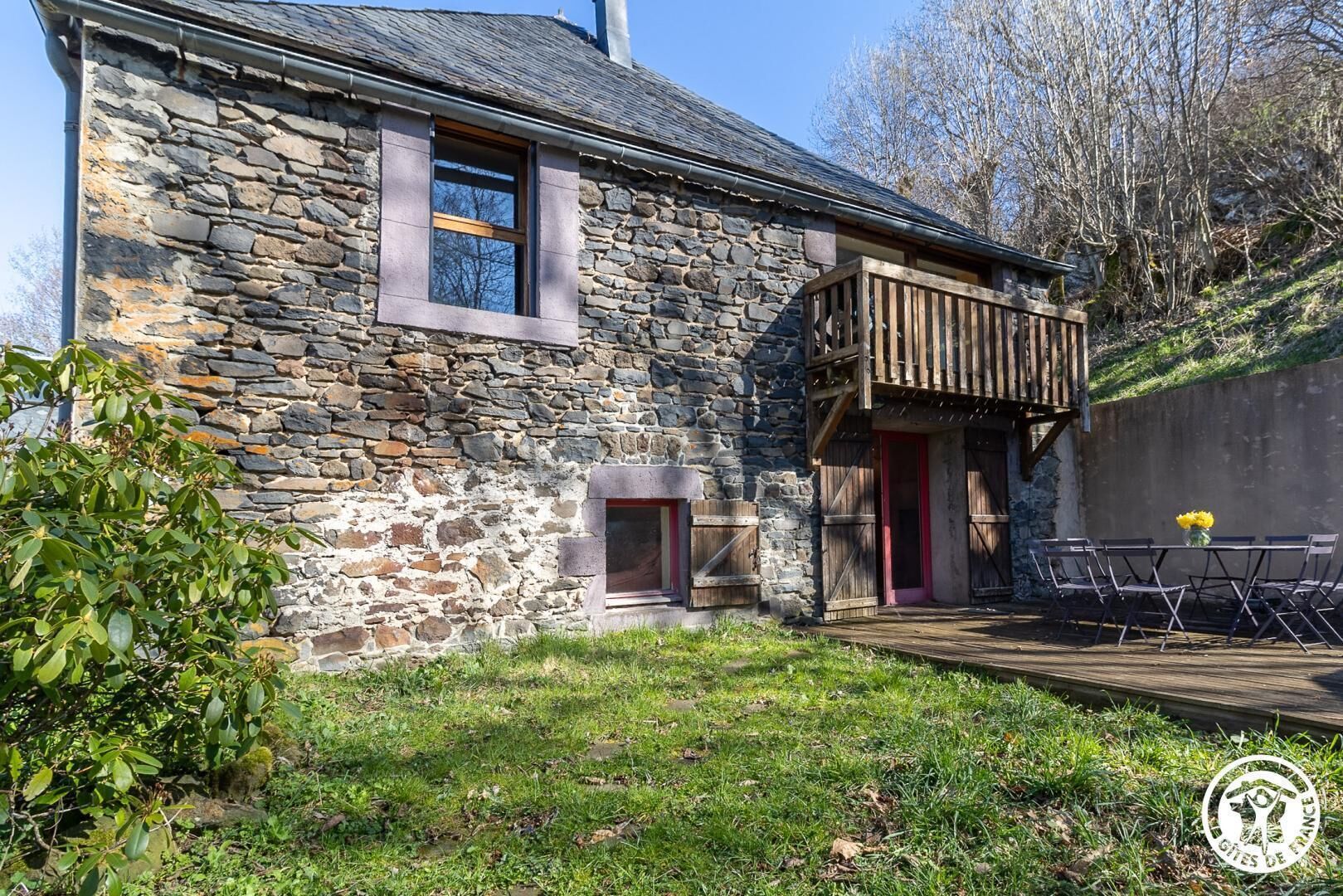 Un bâtiment en pierre doté d’un balcon en bois, d’une petite porte et d’une table avec des chaises à l’extérieur.