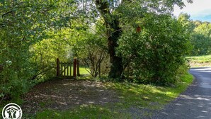 A rural road with a wooden gate, surrounded by dense greenery and trees.