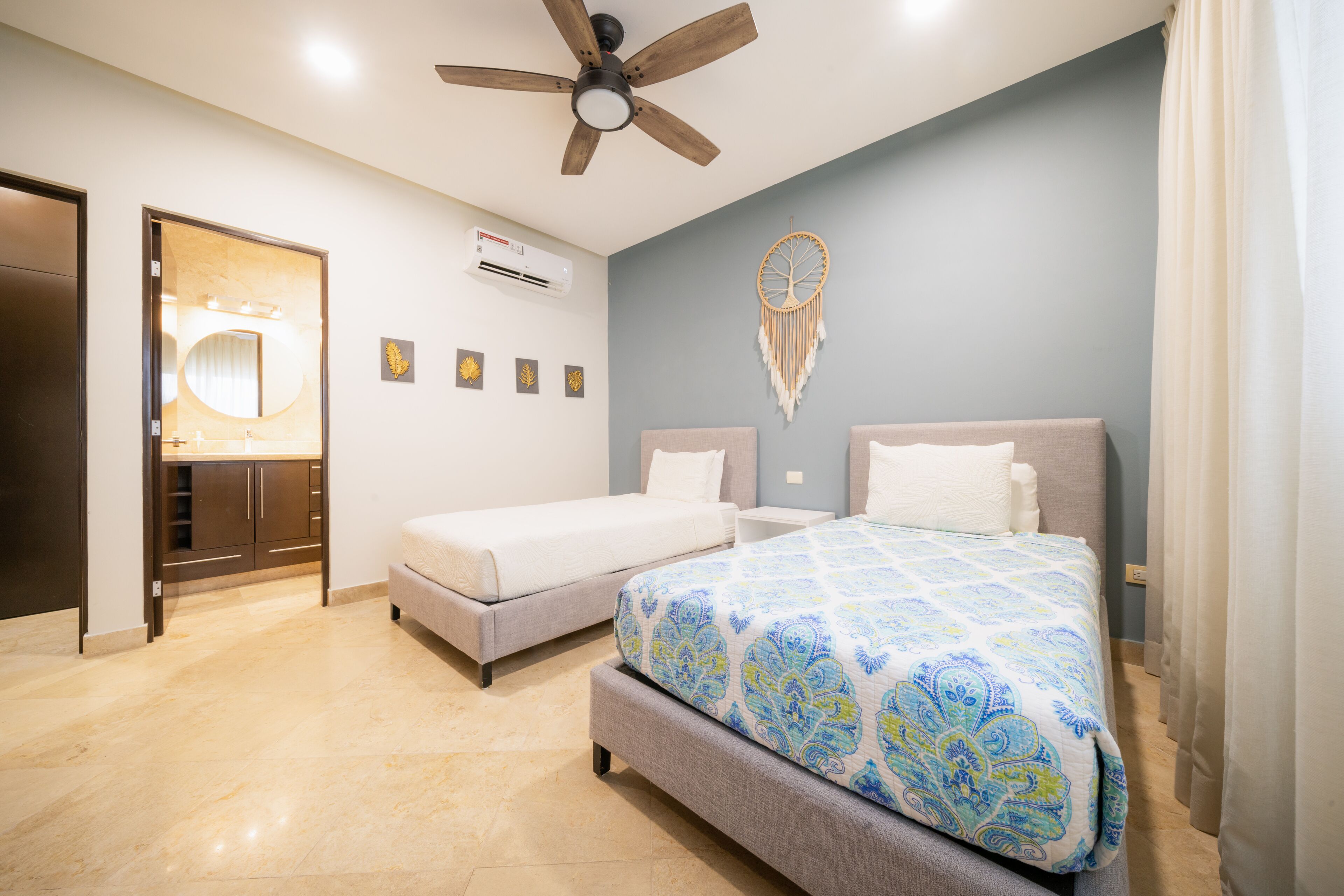 A bedroom with two beds, a ceiling fan, a vanity with a mirror, and a wall-mounted air conditioner.