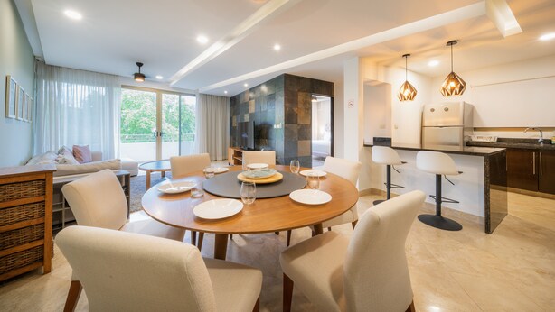 A modern dining area with a round table, chairs, and a kitchen in the background. - Luxury 2 Bedroom Condo at Haab (Playa del Carmen)