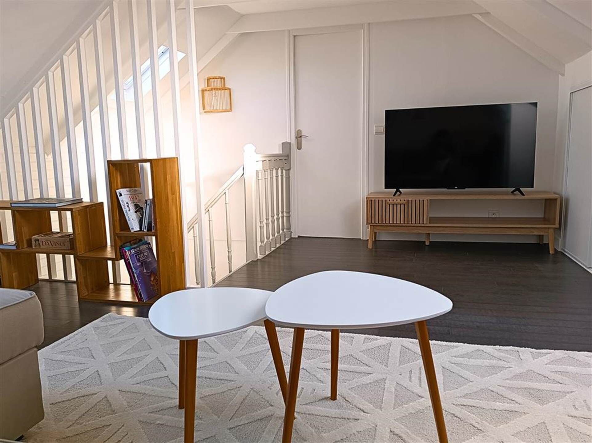 A spacious living room with a large TV, a staircase, and a bookshelf.