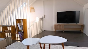Uma sala de estar espaçosa, com uma televisão grande, uma escada e uma estante de livros.
