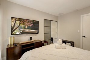 A hotel room with a bed, a flat-screen TV mounted on the wall, a wooden dresser, and a sliding door.