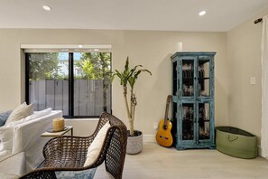 A living room with a sofa, a wicker chair, a potted plant, a guitar, and a blue cabinet. - Saltwater Pool, Firepit & Workspace I 7 min to Brickell (Miami)