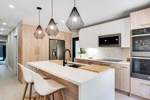 A modern kitchen with a central island, pendant lighting, stainless steel appliances, and a tiled backsplash. - Saltwater Pool, Firepit & Workspace I 7 min to Brickell (Miami)