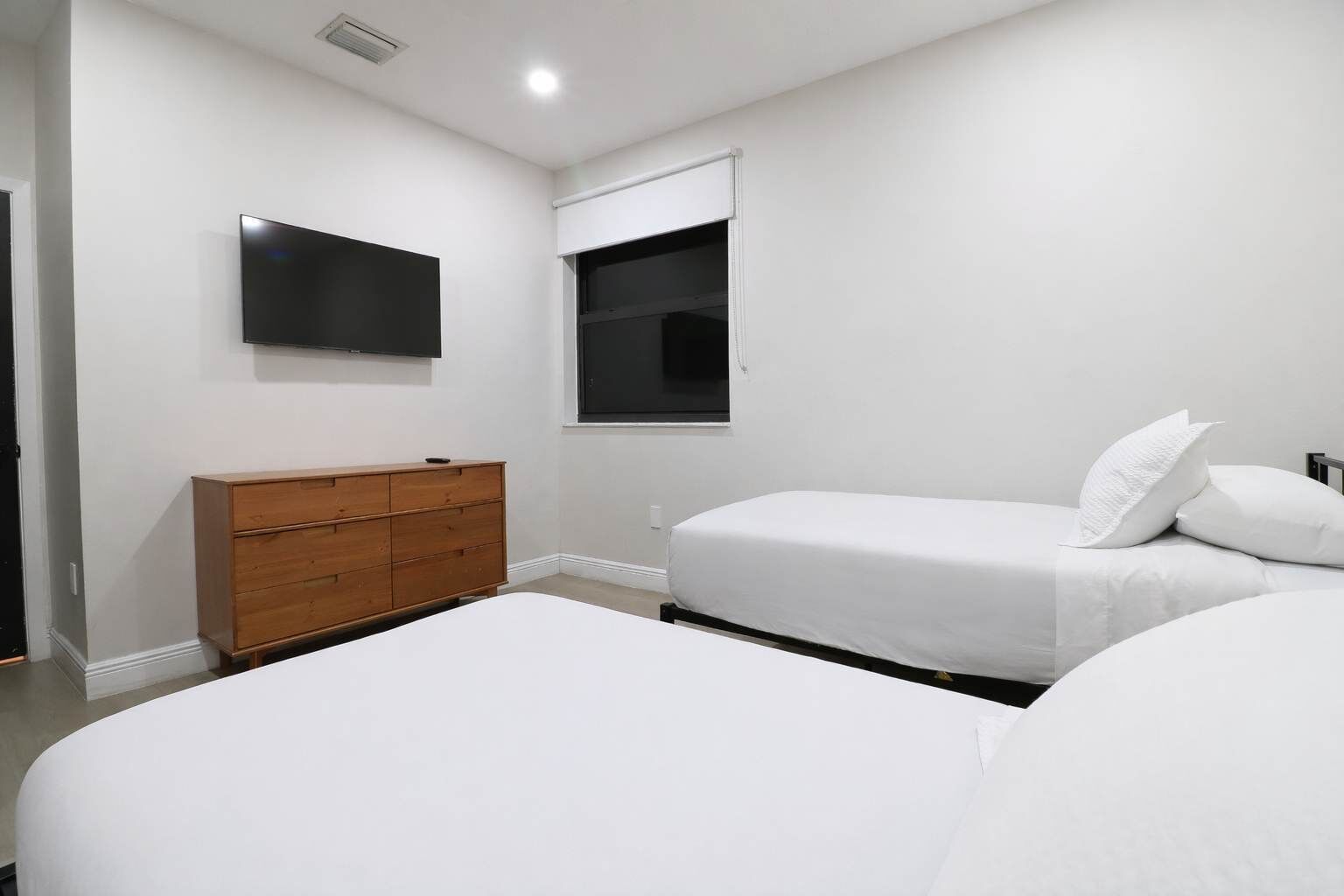 A bedroom with two beds, a wooden dresser, and a TV mounted on the wall.