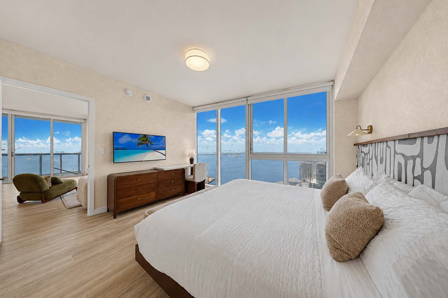 A spacious bedroom with a large bed, a television, a desk, and a view of the ocean.