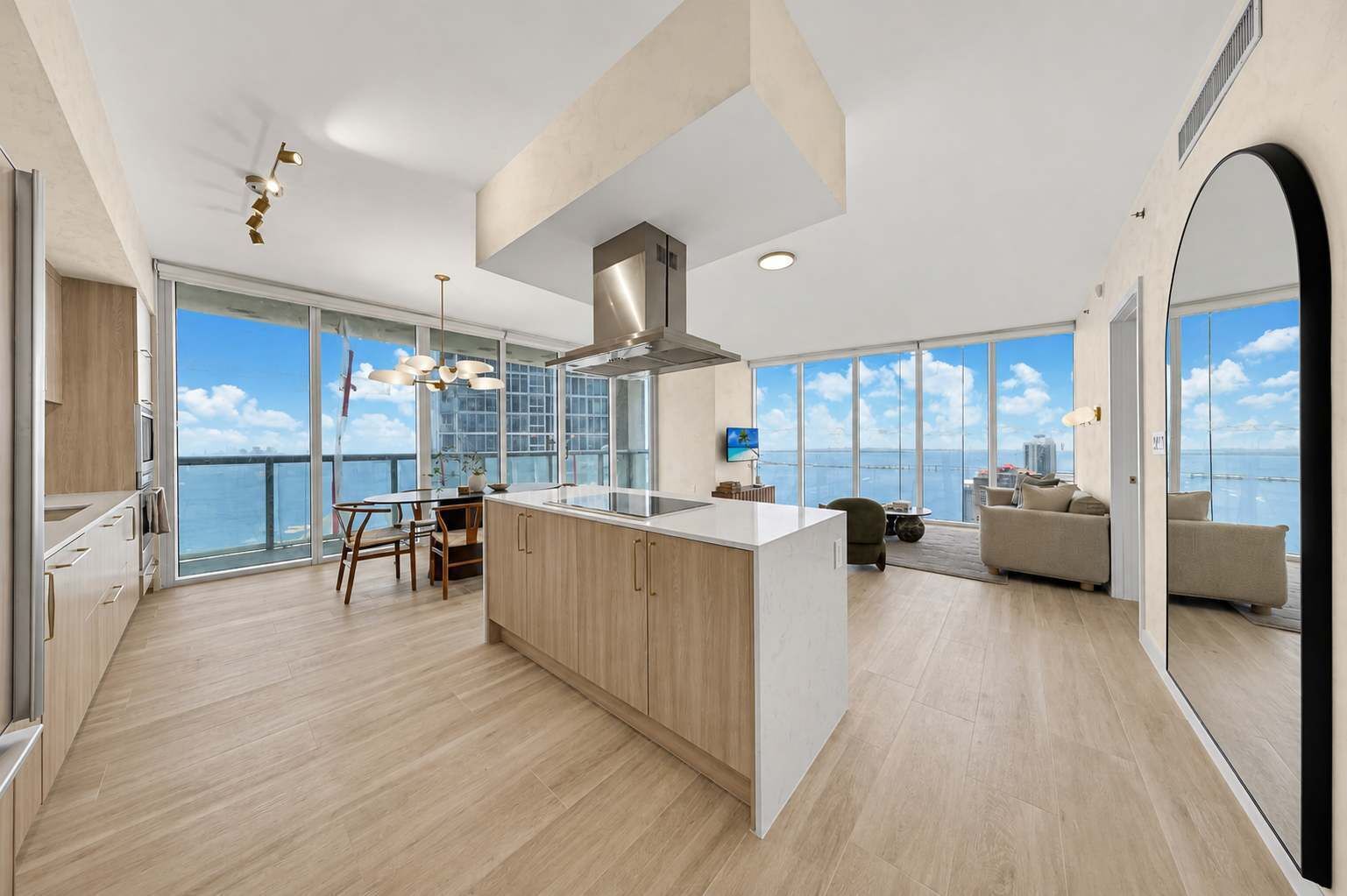 A modern kitchen with a large island, a dining area with a view, and a living space with a sofa and a TV.