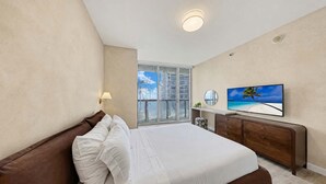 Una camera da letto con un letto grande, una TV e vista sulla spiaggia dalla finestra.