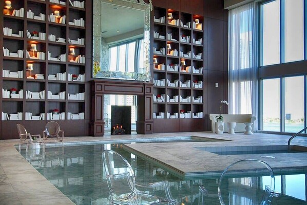 Una biblioteca con estanterías, chimenea y piscina.