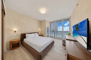 Une chambre d’hôtel avec un grand lit, une télévision, un balcon avec vue et une petite table agrémentée d’une plante.