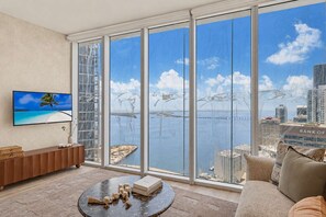 Una sala de estar moderna con un amplio ventanal que da a una vista del frente marítimo y el paisaje urbano.