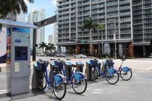 Una estación de Citi Bike con varias bicicletas estacionadas, un quiosco de pagos y un edificio moderno al fondo.