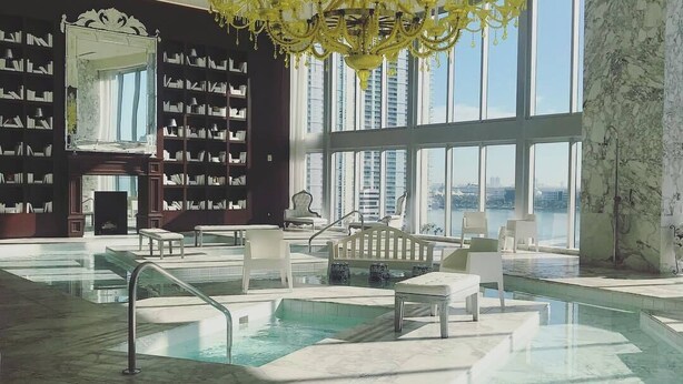A spacious indoor pool area with a large chandelier, marble flooring, and a view of the city through large windows. - Sunrise Water Views I Pool, Spa, Gym & Free Parking (Miami)