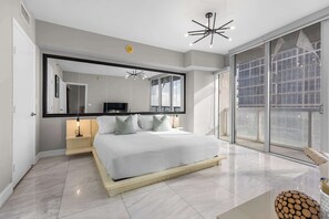 Une chambre moderne avec un grand lit, un miroir, un luminaire au plafond et une vue à travers une porte vitrée.