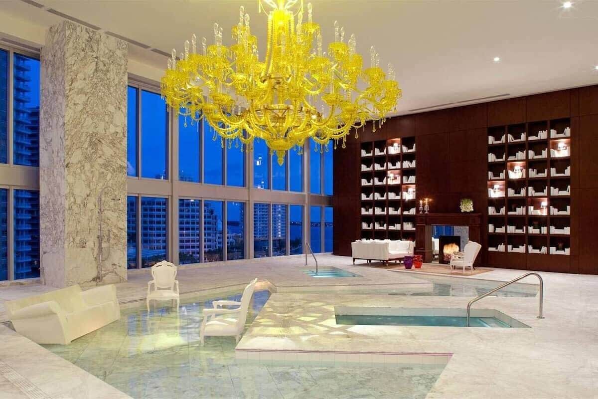 A spacious indoor area with a large pool, a yellow chandelier, and a library with bookshelves.
