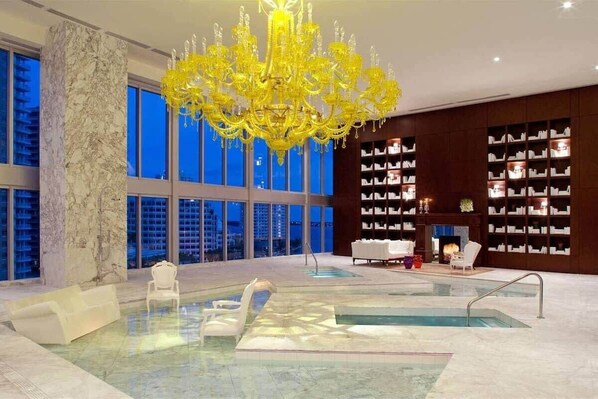 A spacious indoor area with a large pool, a yellow chandelier, and a library with bookshelves.