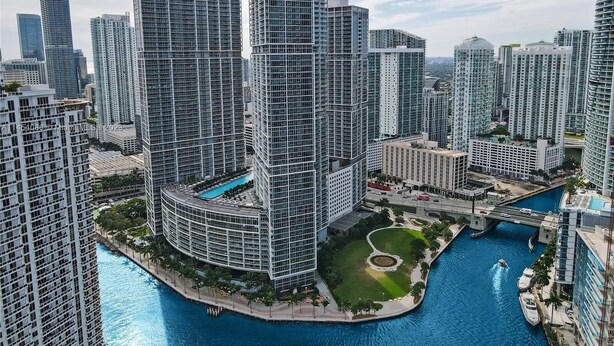 Uma área urbana com arranha-céus e arquitetura moderna, um edifício circular central com piscina e um canal com barcos.