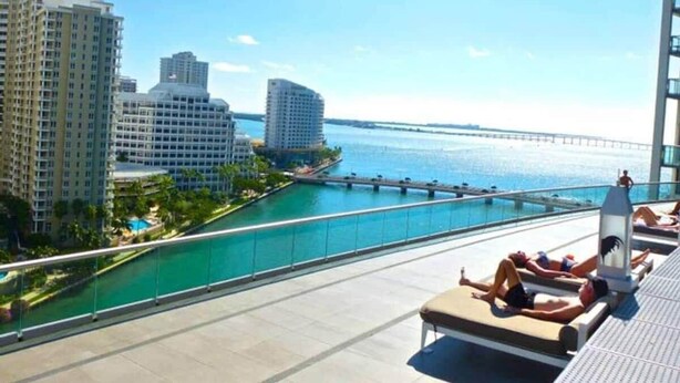 Una piscina en la azotea con vista al océano y a un puente, rodeada de rascacielos.