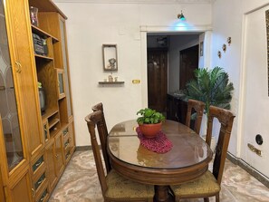 A dining area with a round table, chairs, a wooden cabinet, a potted plant, and a doorway leading to another room.