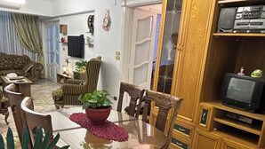 Un comedor con una mesa redonda, sillas, una planta en maceta y un televisor sobre un mueble de madera.