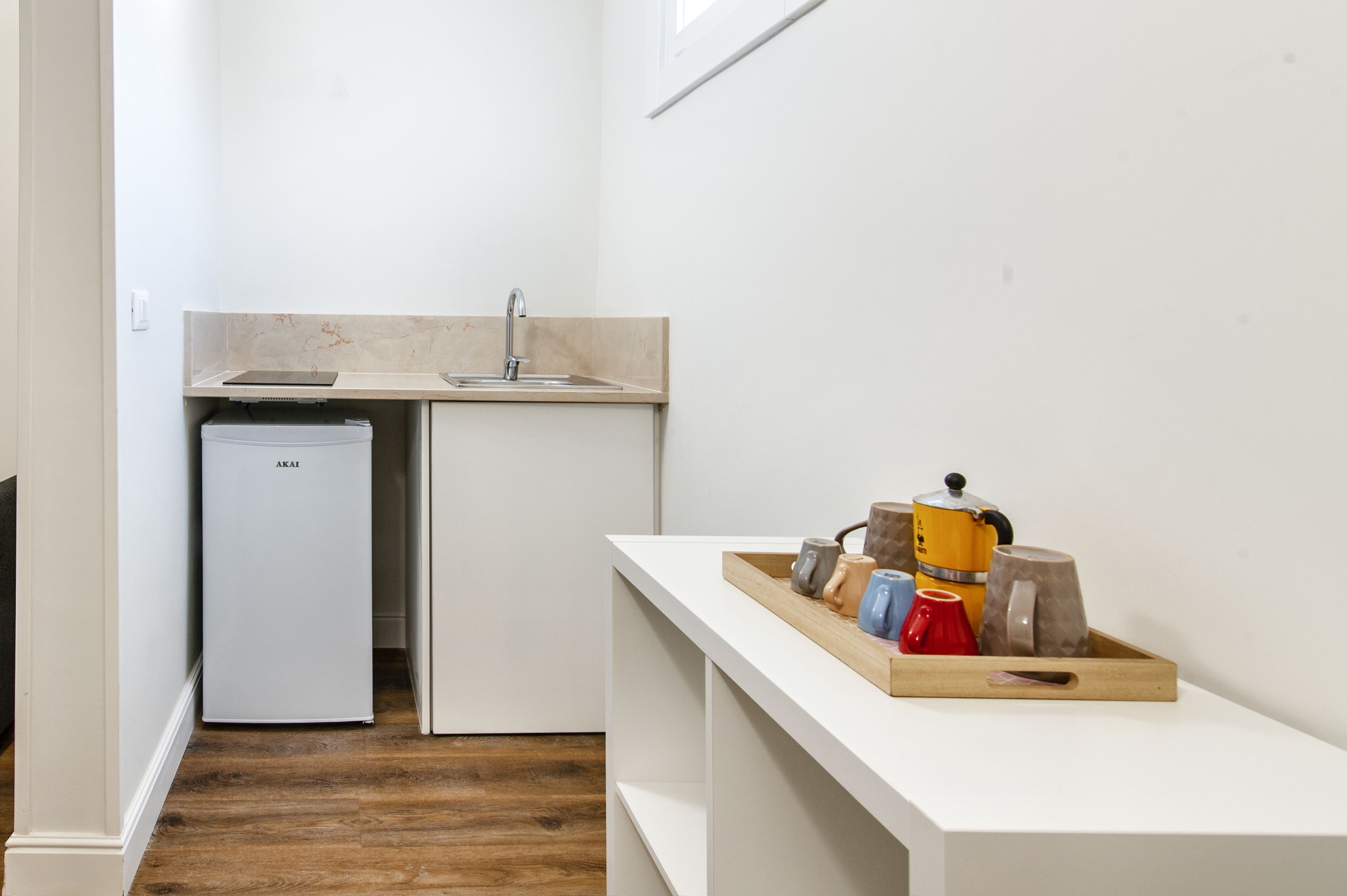A compact kitchen with a refrigerator, sink, and a wooden shelf holding various kitchen items.