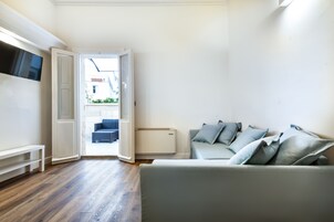 Una sala de estar moderna con un sofá gris, un televisor de pantalla plana montado en la pared y piso de madera.
