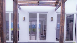 A modern outdoor entrance with stone steps leading to a glass door, wooden pergola overhead, and a white building facade. - Lake Side Deluxe Villa (Nadi)