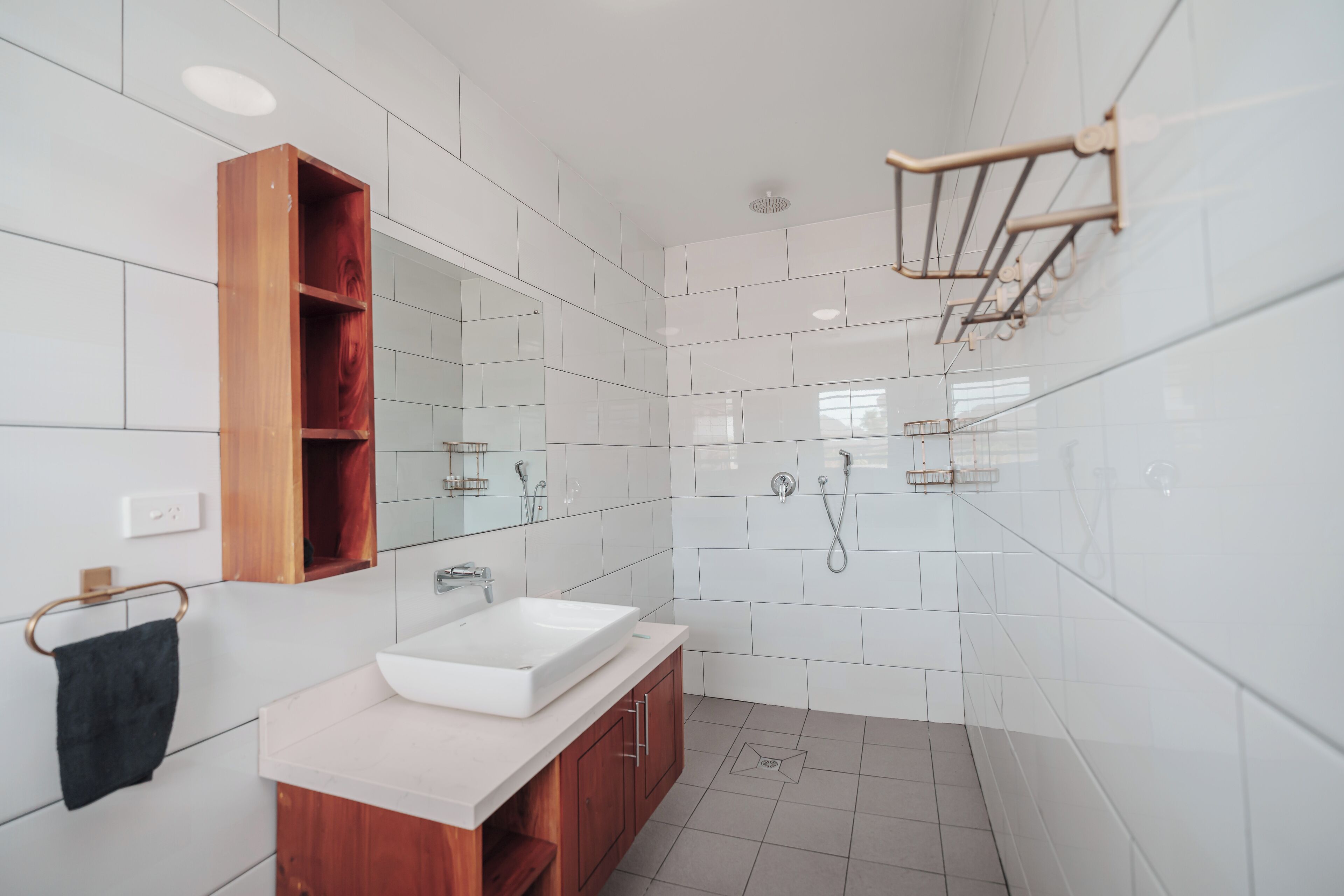 Un baño moderno con tocador de madera, un espejo grande y zona de ducha.