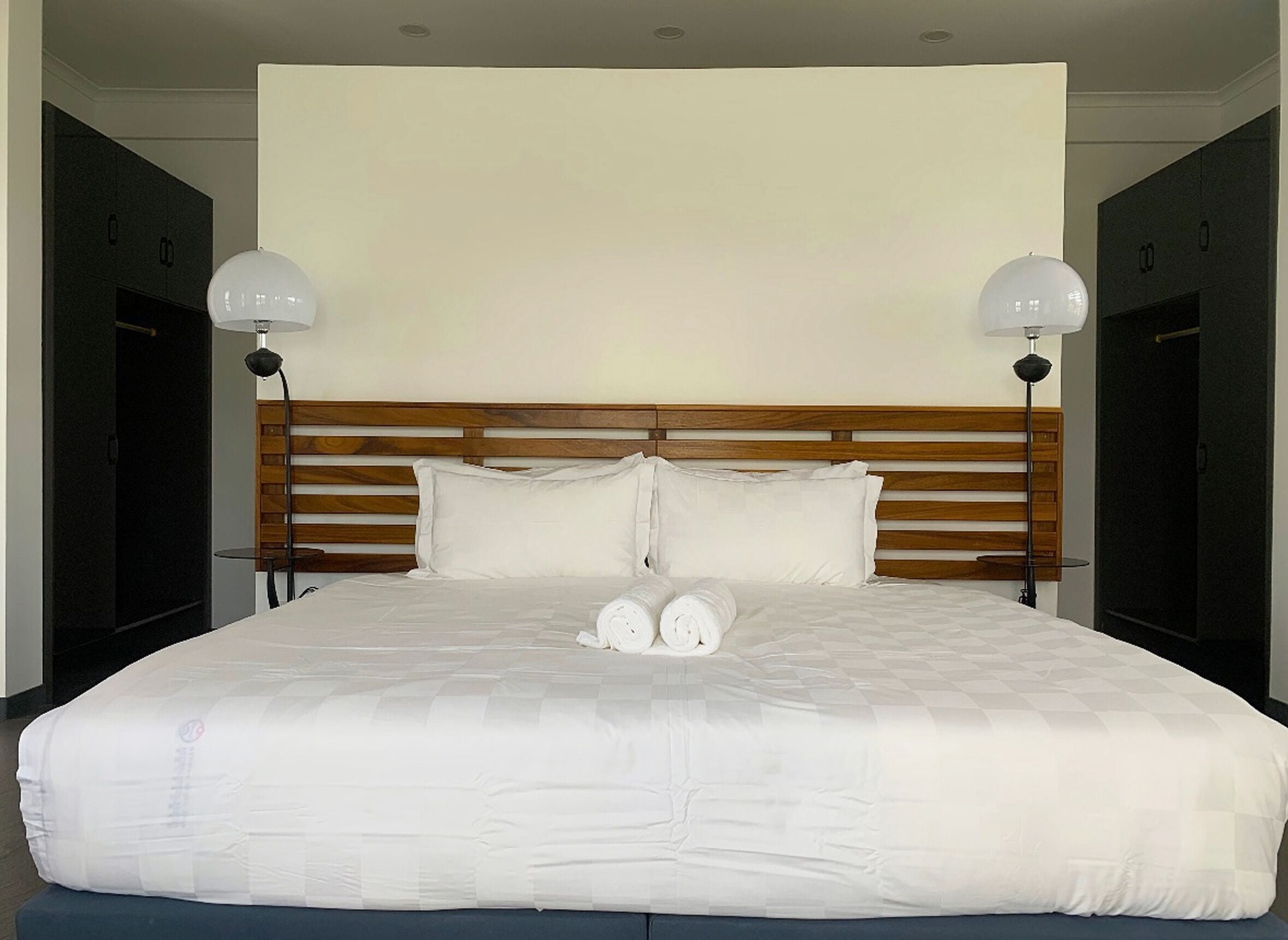 A large bed with a wooden headboard, two bedside lamps, and rolled towels on the bed.