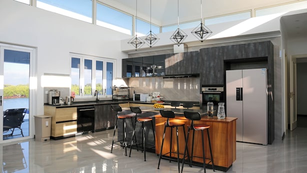 A modern kitchen with a central island, bar stools, and a large refrigerator. - Lake Side Deluxe Villa (Nadi)