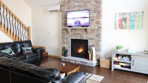 Een woonkamer met een stenen openhaard, een zwarte leren bank en een televisie die boven de openhaard is bevestigd.