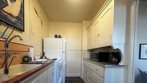 A narrow kitchen with white cabinets, a white refrigerator, a microwave, and a coffee maker on the countertop. - Vintage Studio in Belltown-Space Needle (Seattle)