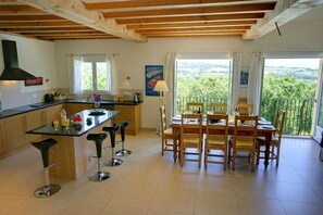 Una cocina con una isla central, taburetes de bar, una mesa de comedor con sillas y vistas amplias a través de grandes ventanales.