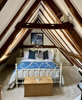 Un dormitorio con techo inclinado, una cama con estructura de metal blanco, una colcha azul y blanca a rayas y un aparador de madera.