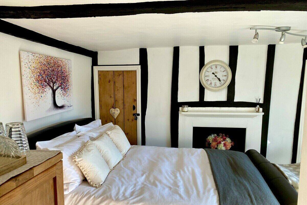 A bedroom with a bed, a clock, a fireplace, and a painting on the wall.