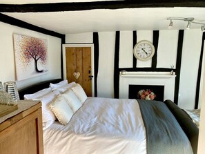 A bedroom with a bed, a clock, a fireplace, and a painting on the wall.