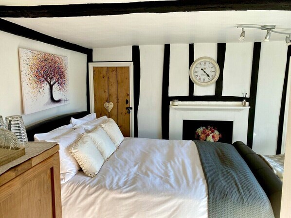 Um quarto com uma cama, um relógio, uma lareira e um quadro na parede.
