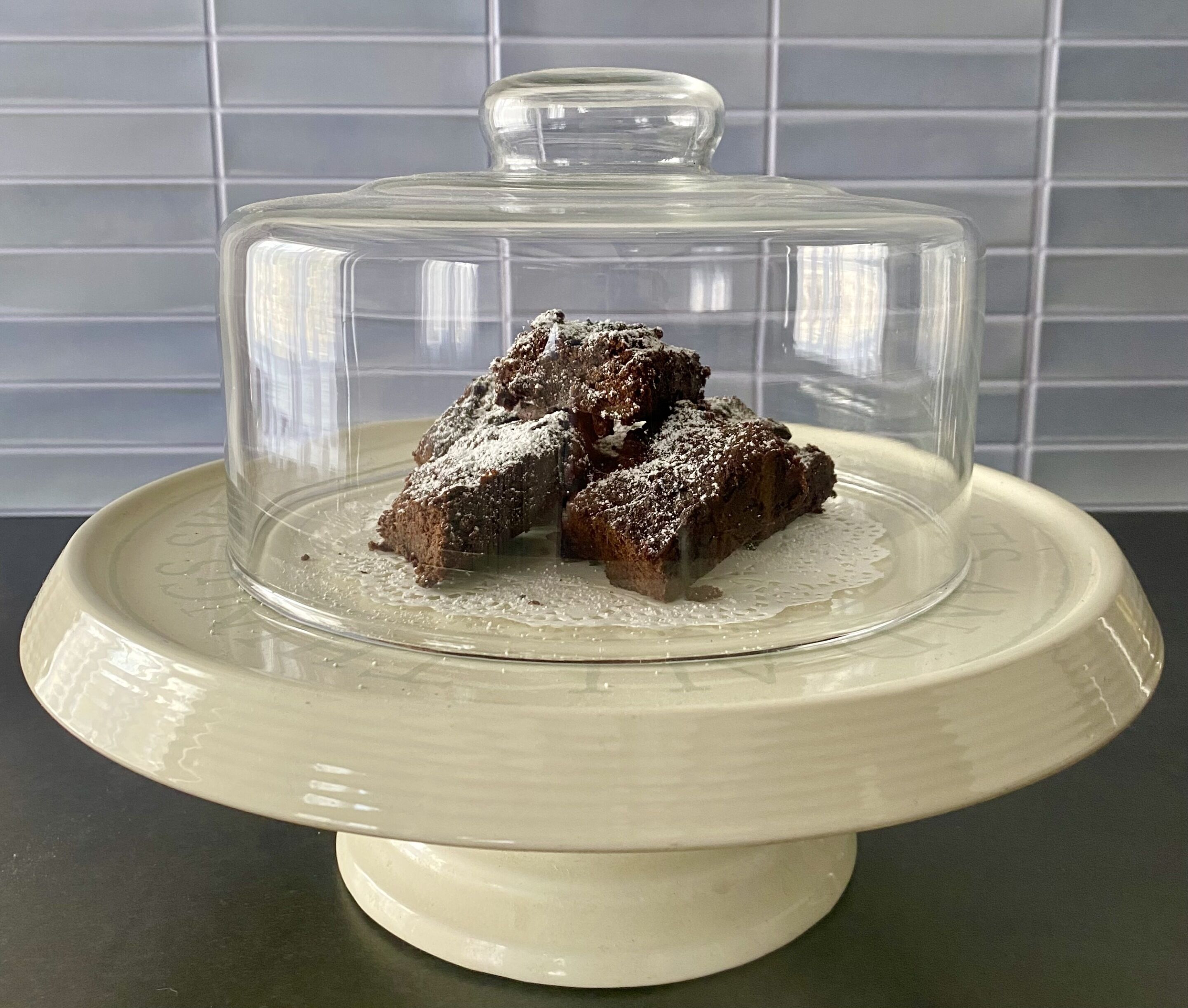 A dessert covered with a glass dome on a ceramic plate.