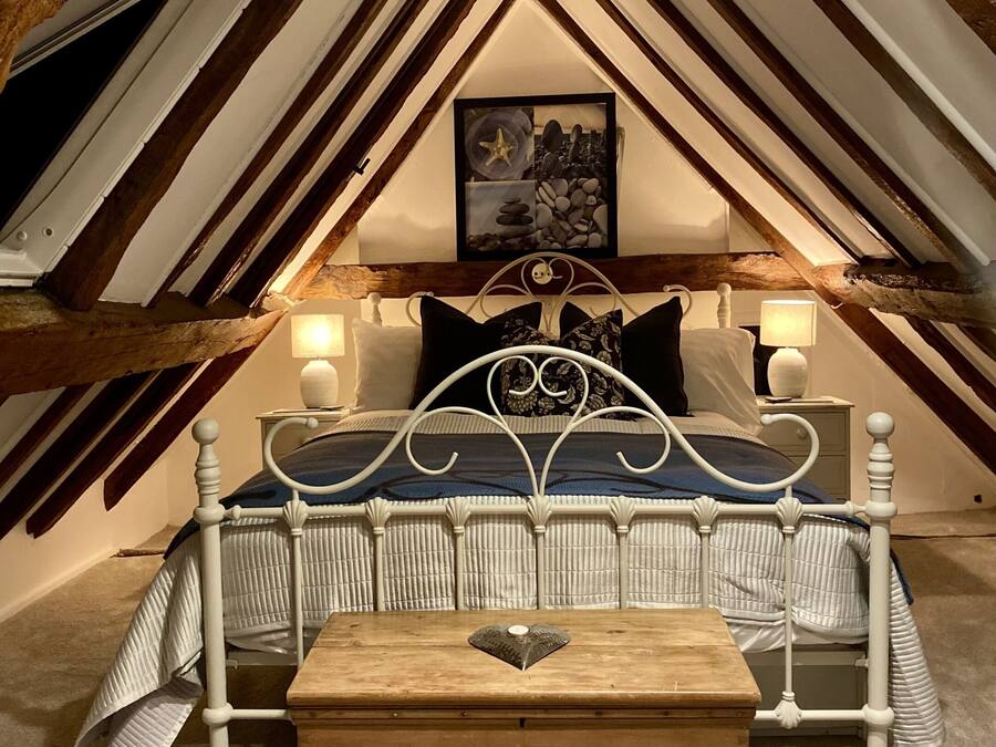 Accogliente camera mansardata con un letto, lampade sui comodini e un baule di legno.