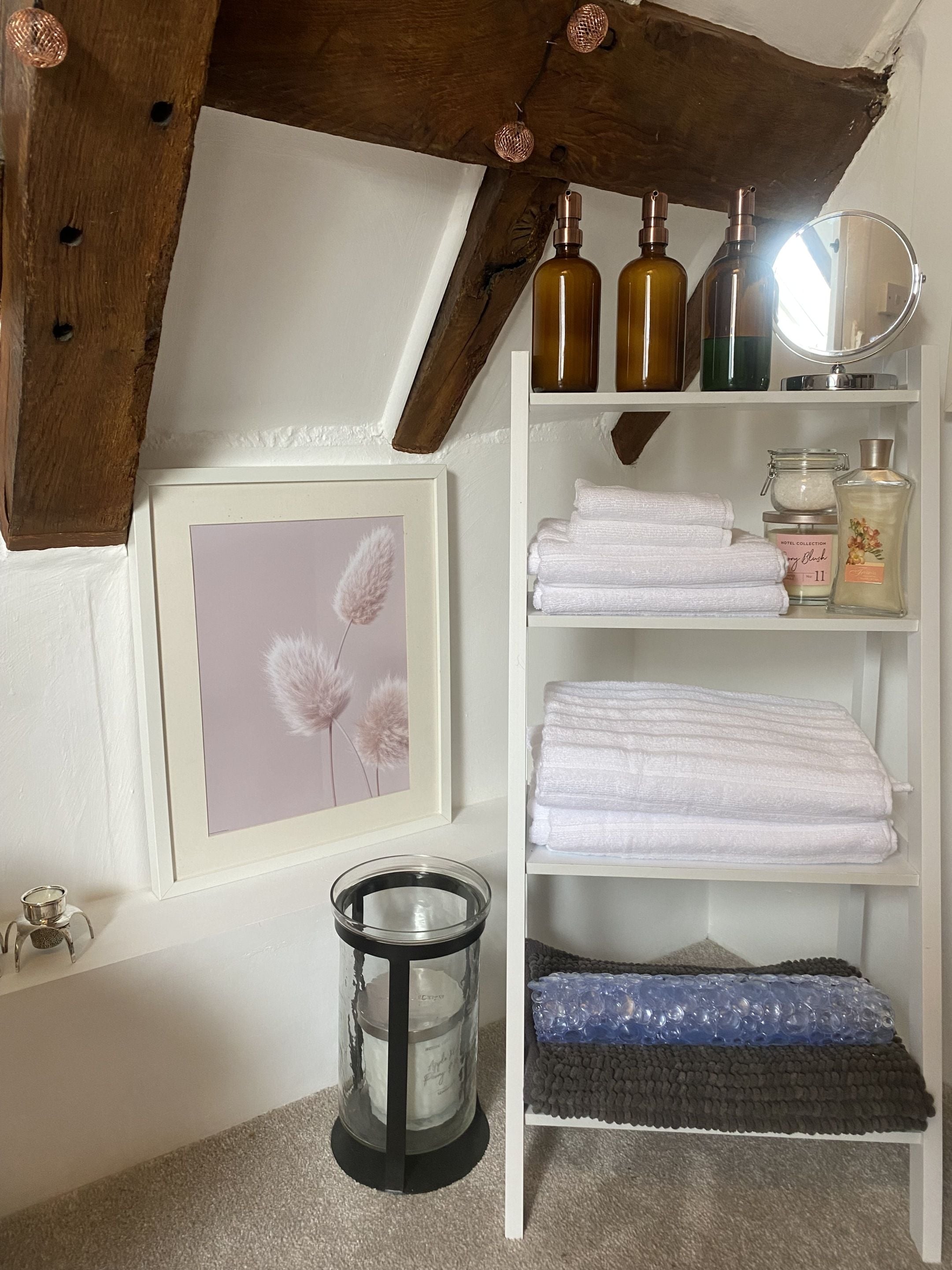 Une salle de bain avec un plafond en bois, un tableau encadré, une étagère avec des serviettes et des articles de toilette, et un porte-bougie.
