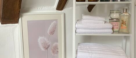 Une salle de bain avec un plafond en bois, un tableau encadré, une étagère avec des serviettes et des articles de toilette, et un porte-bougie.