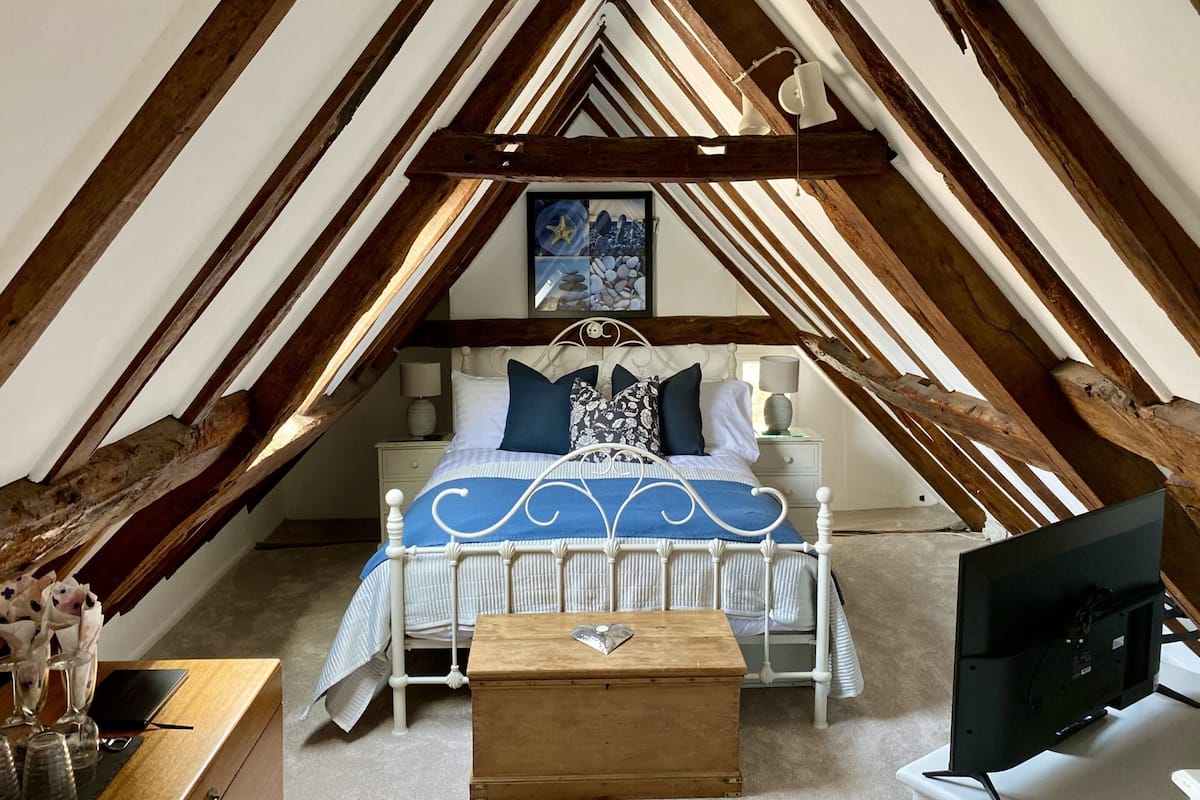 A bedroom with a sloped ceiling, a bed with a white frame, and a wooden bedside table.