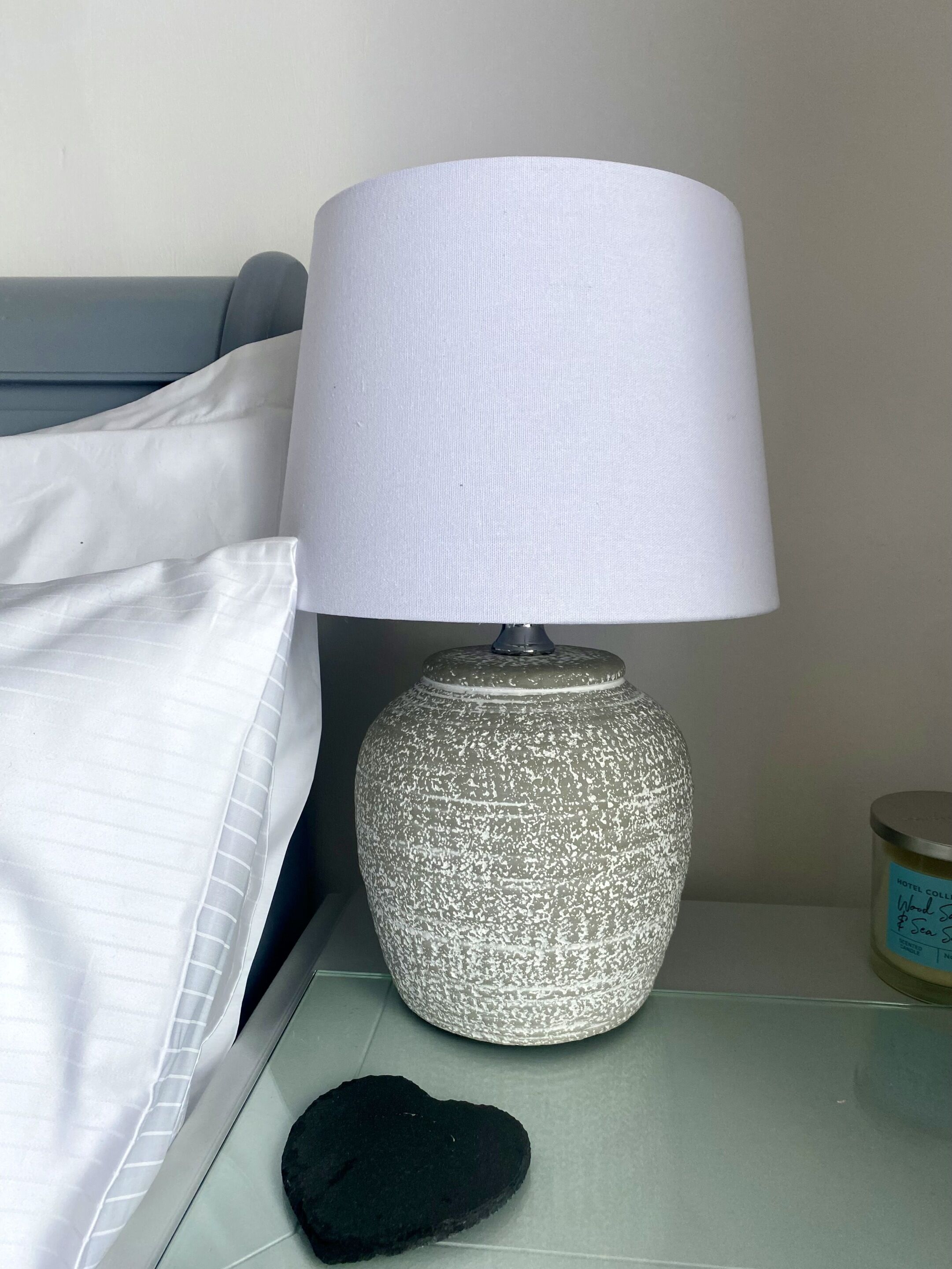 A lamp with a textured base and a white lampshade on a bedside table.