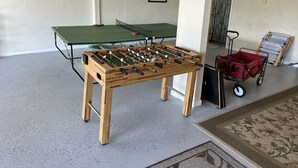 A room with a foosball table, ping pong table, and a red suitcase. - Waterfront 4 BR retreat at the sound side and only 100 steps to the ocean beach. (Emerald Isle)