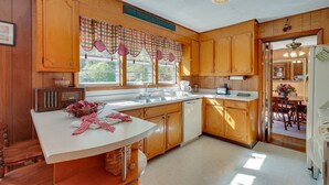 A kitchen with wooden cabinets, a white countertop, a radio, and a window with checkered curtains. - Haysi Nature Getaway w/ Fire Pit & On-Site Creek! (Haysi)